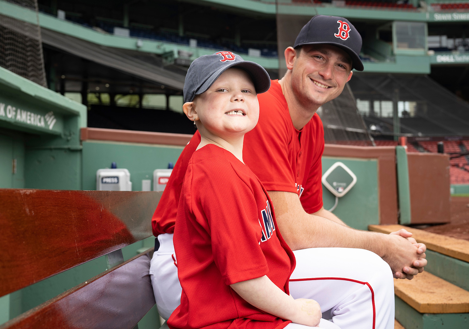 Dana-Farber Jimmy Fund Clinic patient Lily sits in the dugout with Red Sox pitcher Garrett Whitlock at Fenway Park