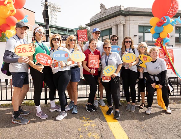 A Boston Marathon Jimmy Fund Walk corporate team poses for a photo with signs and balloons