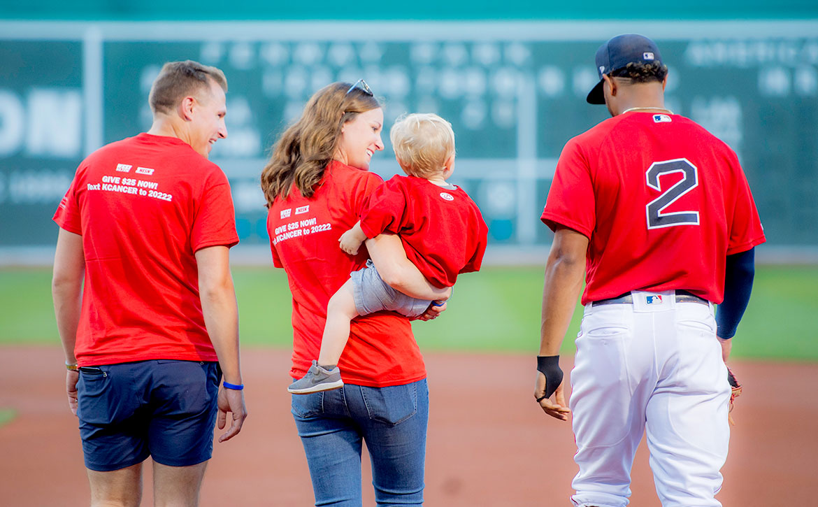 A Dana-Farber patient and family join Red Sox player, Xander Bogaerts, in front of the Green Monster